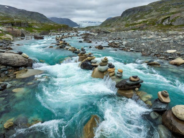 Fast-flowing turquoise glacial meltwater rushing over rounded cobbles in a high Norwegian valley