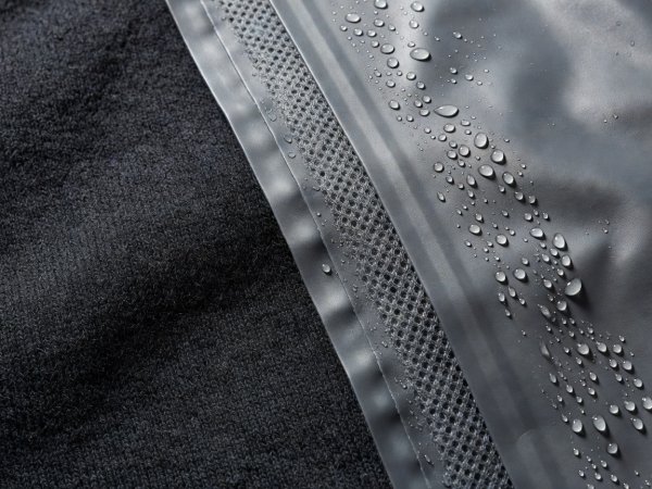 Close-up texture of dark merino wool weave next to a water-beaded three-layer waterproof hardshell membrane